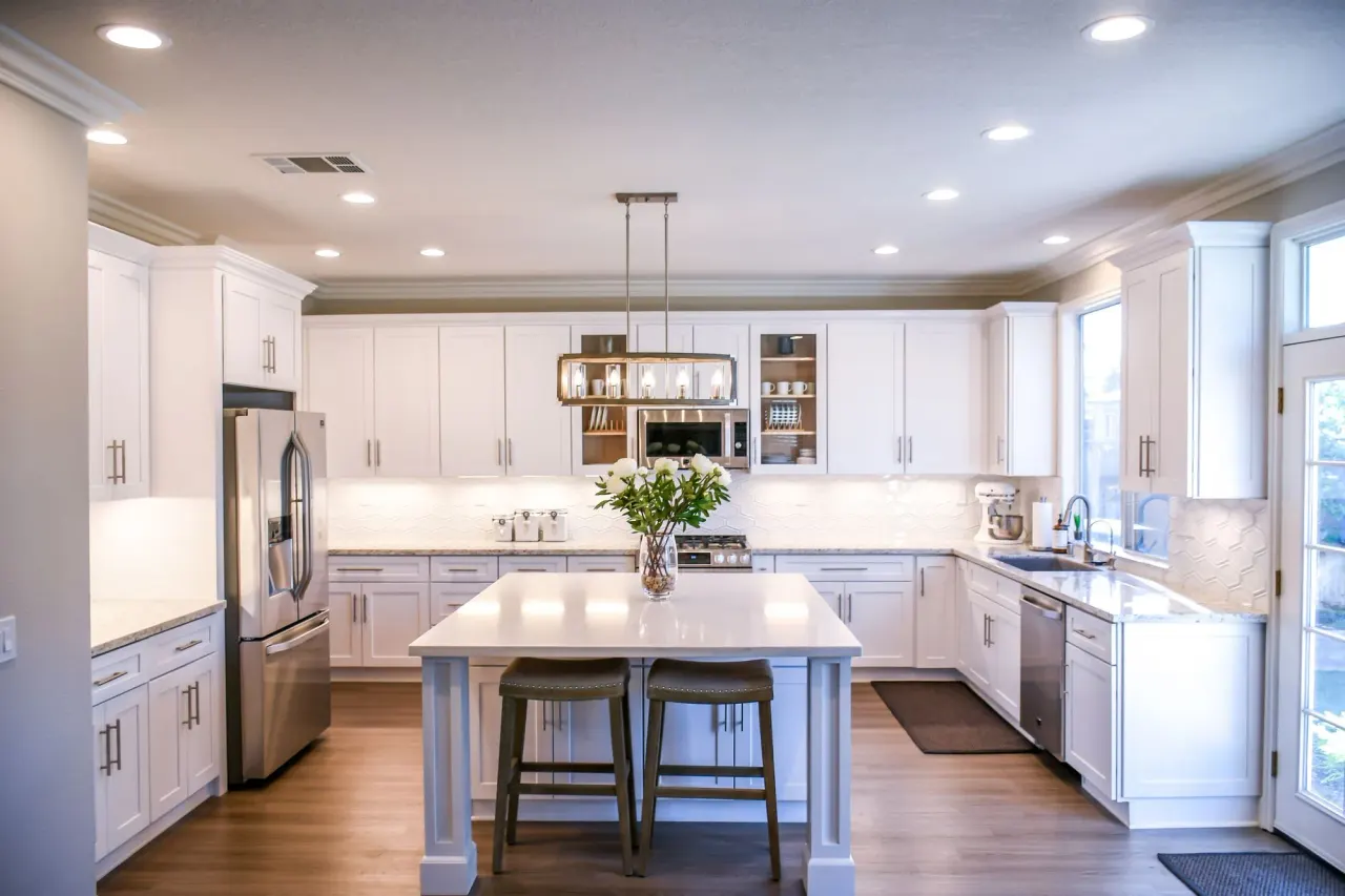 Cocina blanca con isla central, taburetes y suelo de madera